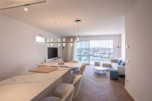 Ein modernes Wohnzimmer mit einer Couch, einer Essecke mit Tisch und Stühlen und Blick auf eine Marina durch große Fenster.