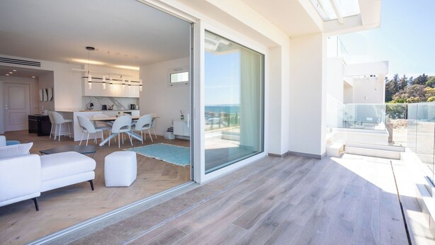 Un interior moderno con comedor, cocina y puerta de cristal que da a un balcón con vistas.
