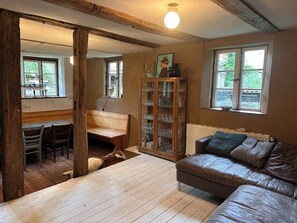 Ein gemütliches Wohnzimmer mit Holzboden, einer Ledersofa, einer Vitrine und einem Essbereich mit Stühlen und einem Tisch.