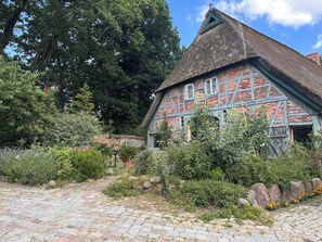 A traditional half-timbered house with a thatched roof, surrounded by a garden with various plants and flowers. - Living Under a Thatched Roof (Toppenstedt)