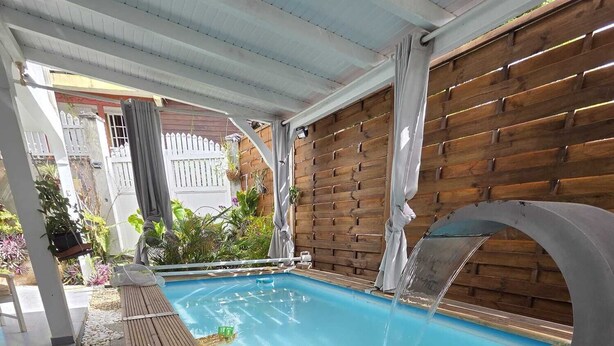 A swimming pool with a wooden deck, surrounded by a wooden fence and a covered area with a metal roof. - Kaz Détente, a 3-bedroom house with a hot tub, just 5 minutes from the beach! (Pointe-Noire)