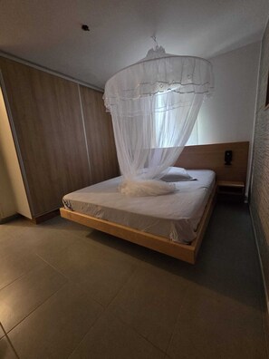 Ein Schlafzimmer mit einem Bett, einem Baldachin, einem Nachttisch und einem an der Wand befestigten Wecker.