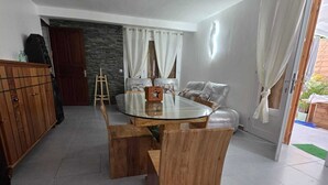 A dining area with a glass-top table and wooden chairs, a stone wall, and a door leading outside. - Kaz Détente, a 3-bedroom house with a hot tub, just 5 minutes from the beach! (Pointe-Noire)