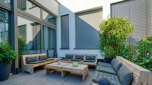 Un área de estar exterior moderna con mobiliario de madera y una estatua de Buda.