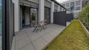 Un moderno edificio residencial con un patio que cuenta con una mesa, sillas, un muro cortina corredizo y un jardín cercado.
