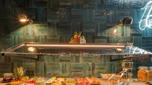 Montaje de bufé con distintos alimentos y un letrero de neón en la pared.