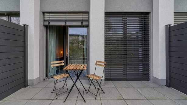 Un patio exterior moderno con una mesa, sillas, una puerta corredera y un muro exterior gris.