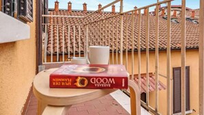 Ein Balkon mit Ziegeldach, einem Metallgeländer und einem Tisch mit einem Buch und einer Tasse.