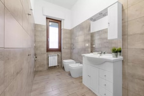 A modern bathroom with a shower, toilet, and sink, featuring light-colored tiles and a window. - MA26 [San Siro] Large - New apartment - (Lombardia)