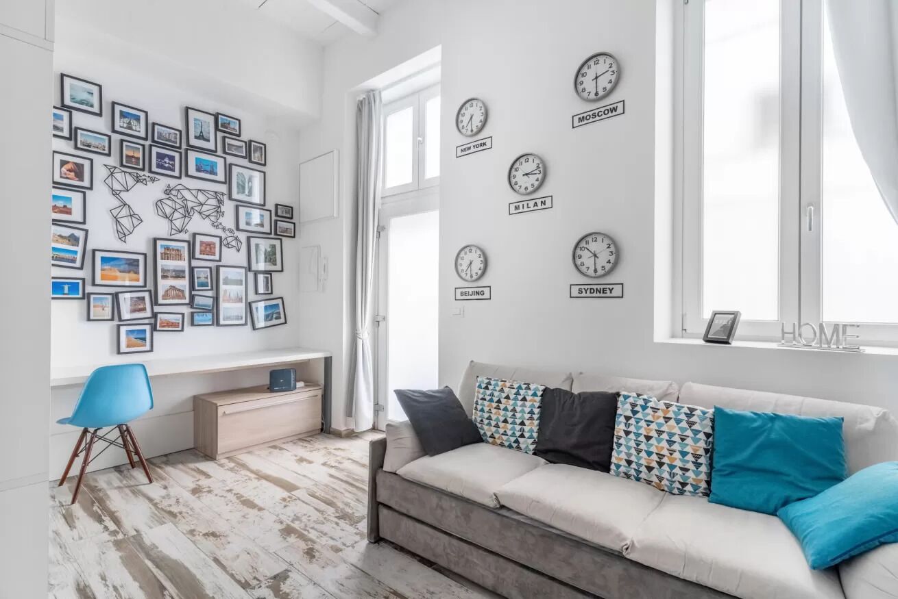 A modern living room with a sofa, a desk, and a wall with clocks labeled with city names.