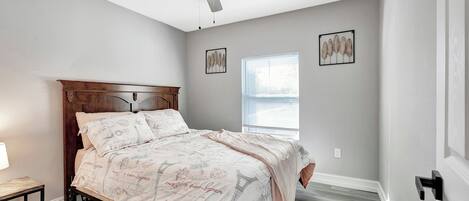A bedroom with a bed, ceiling fan, window, and artwork on the walls.
