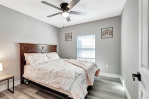 Ein Schlafzimmer mit Bett, Deckenventilator, Fenster und Kunstwerken an den Wänden.