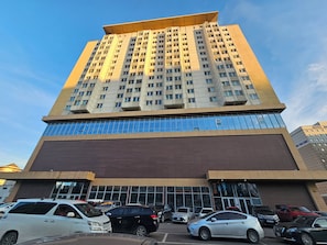 Ett hotell med flera våningar, en modern fasad, stora fönster och en parkeringsplats med olika typer av bilar.