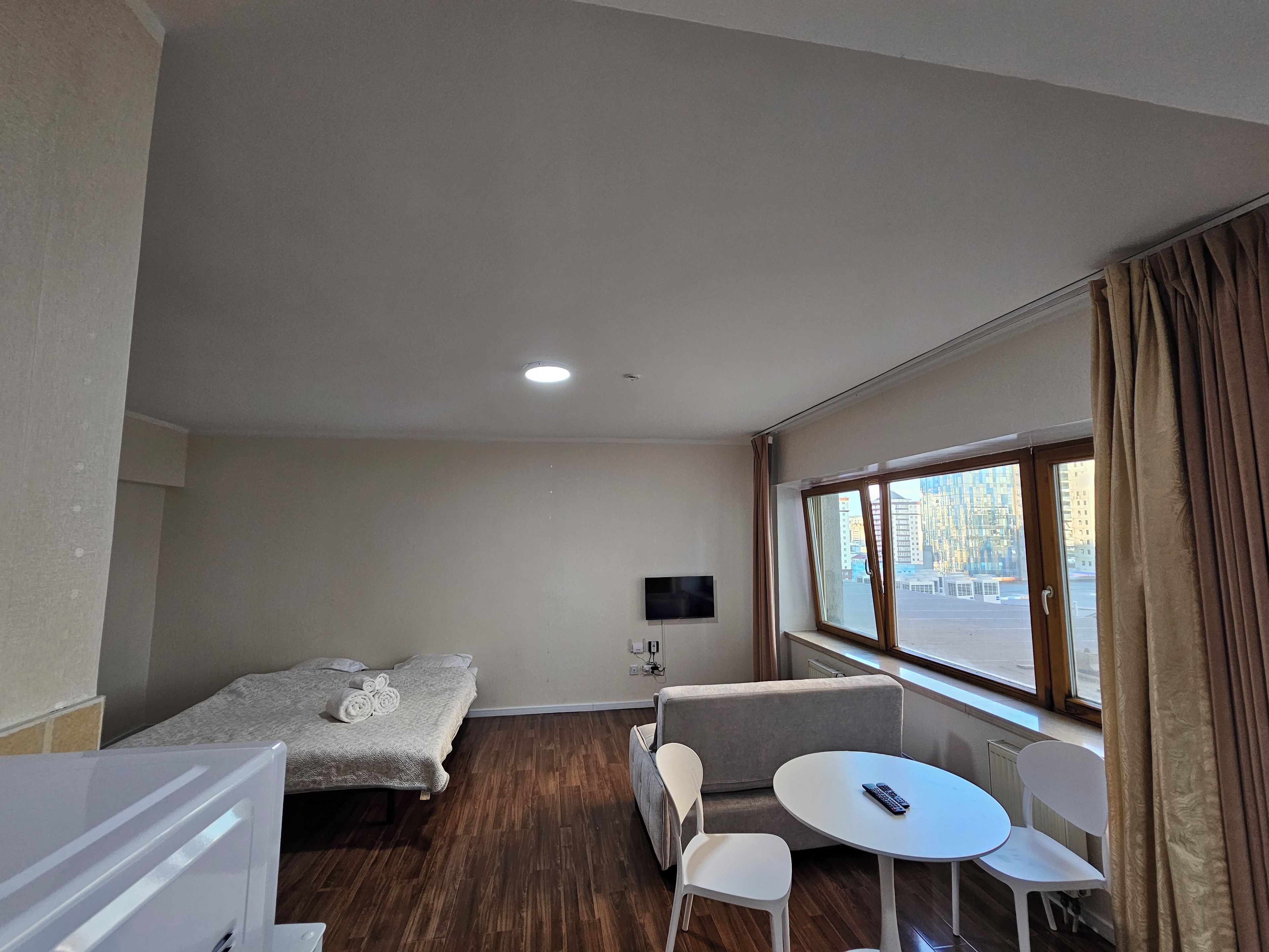 A hotel room with a bed, a sofa, a small table, a TV, and a window with curtains.