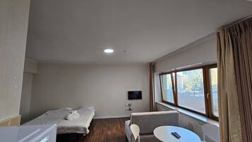 A hotel room with a bed, a sofa, a small table, a TV, and a window with curtains.