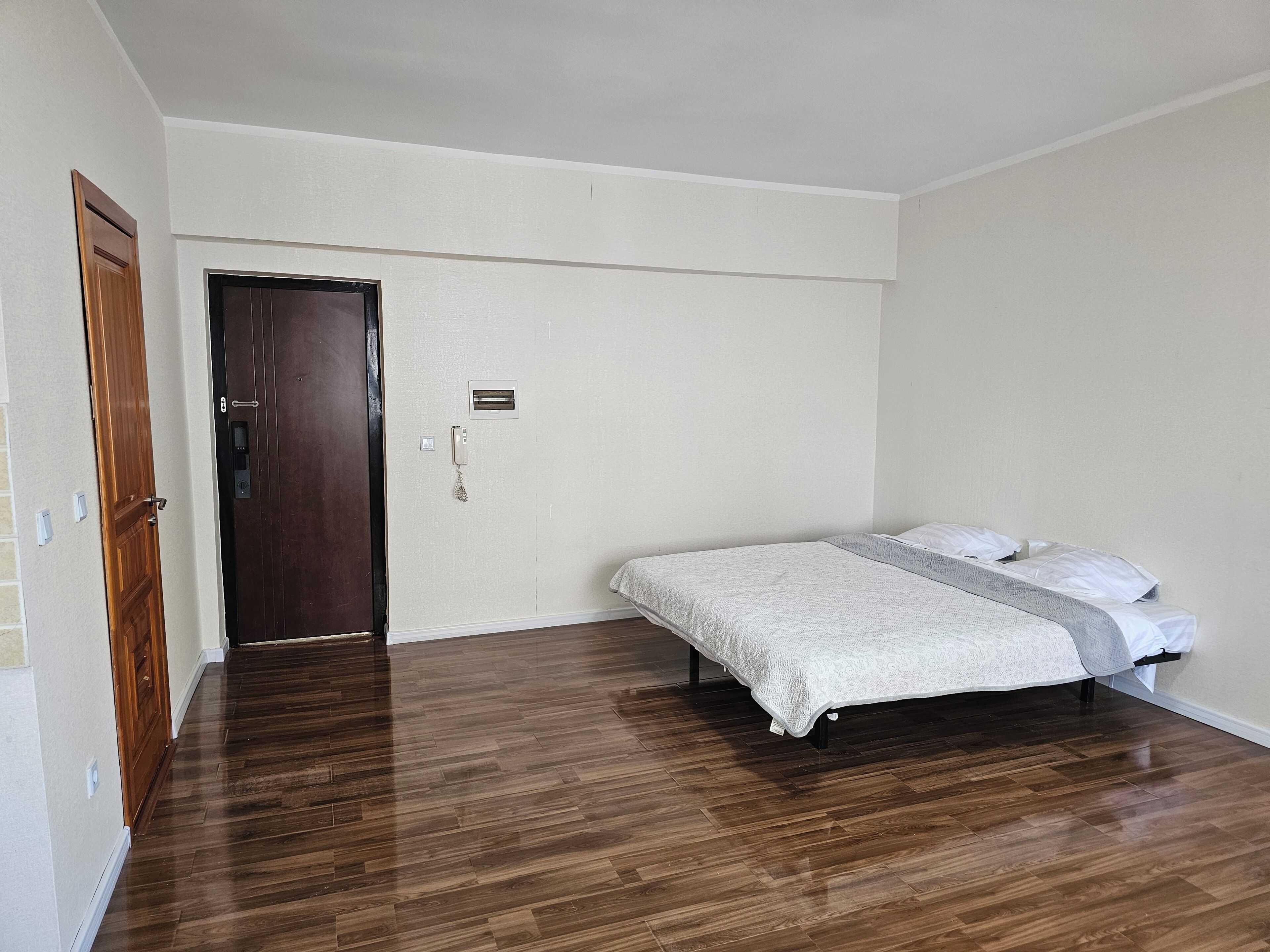 Ein Schlafzimmer mit einem Bett, einer Holztür und einem Lichtschalter an der Wand.