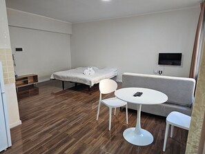 A modern, well-lit room with a bed, a sofa, a small round table, and a TV mounted on the wall. - Max Central City Apartment (Ulaanbaatar)