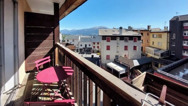 A balcony with a table and chairs, a wooden railing, and a view of buildings and mountains. - Apartment on the 3rd floor, located right in the center of Font-Romeu (Font-Romeu-Odeillo-Via)