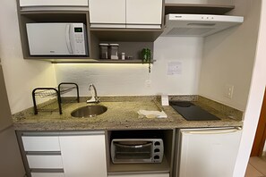 Een kleine keuken met een magnetron, spoelbak en een ingebouwde oven.