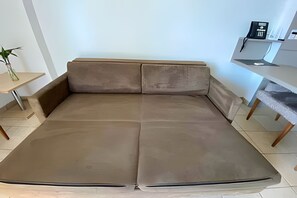 A modern, minimalist living room with a large, neutral-colored sofa, a small side table, and a shelving unit. - SHB Paraíso Frente ao Oceano (Santos)
