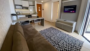 Moderni olohuone, jossa on sohva, kuviollinen matto, televisio sekä keittiöalue, jossa on kaappeja ja ruokapöytä.