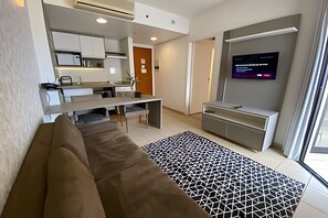 Una sala de estar moderna con un sofá, un tapete estampado, un televisor y una zona de cocina con armarios y una mesa de comedor.