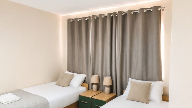 A hotel room with two beds, a nightstand with lamps, and a curtain. - Stylish 3BR House | Free WiFi & Parking | Sleeps 5 | Manchester (Little Hulton)