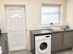 A compact kitchen with a washing machine, a sink, and a window with blinds.