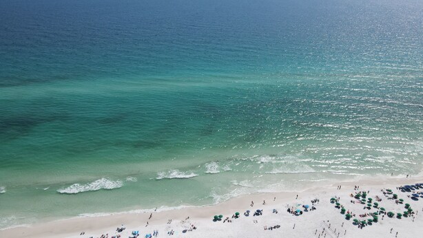 Ein Strand mit klarem türkisblauem Wasser, einem sandigen Ufer und zahlreichen Sonnenschirmen.