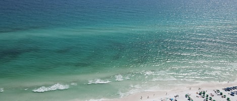 Una playa con agua turquesa transparente, una orilla arenosa y numerosas sombrillas.