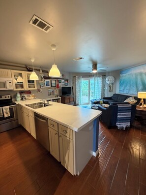 A kitchen with a central island, white cabinets, and a dining area with a sofa and a lamp. - Beach Condo~Steps from Beach~Sleeps 4~Pool~Hot Tub~ (Miramar Beach)
