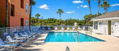 A swimming pool with lounge chairs, a lifeguard tower, and palm trees.
