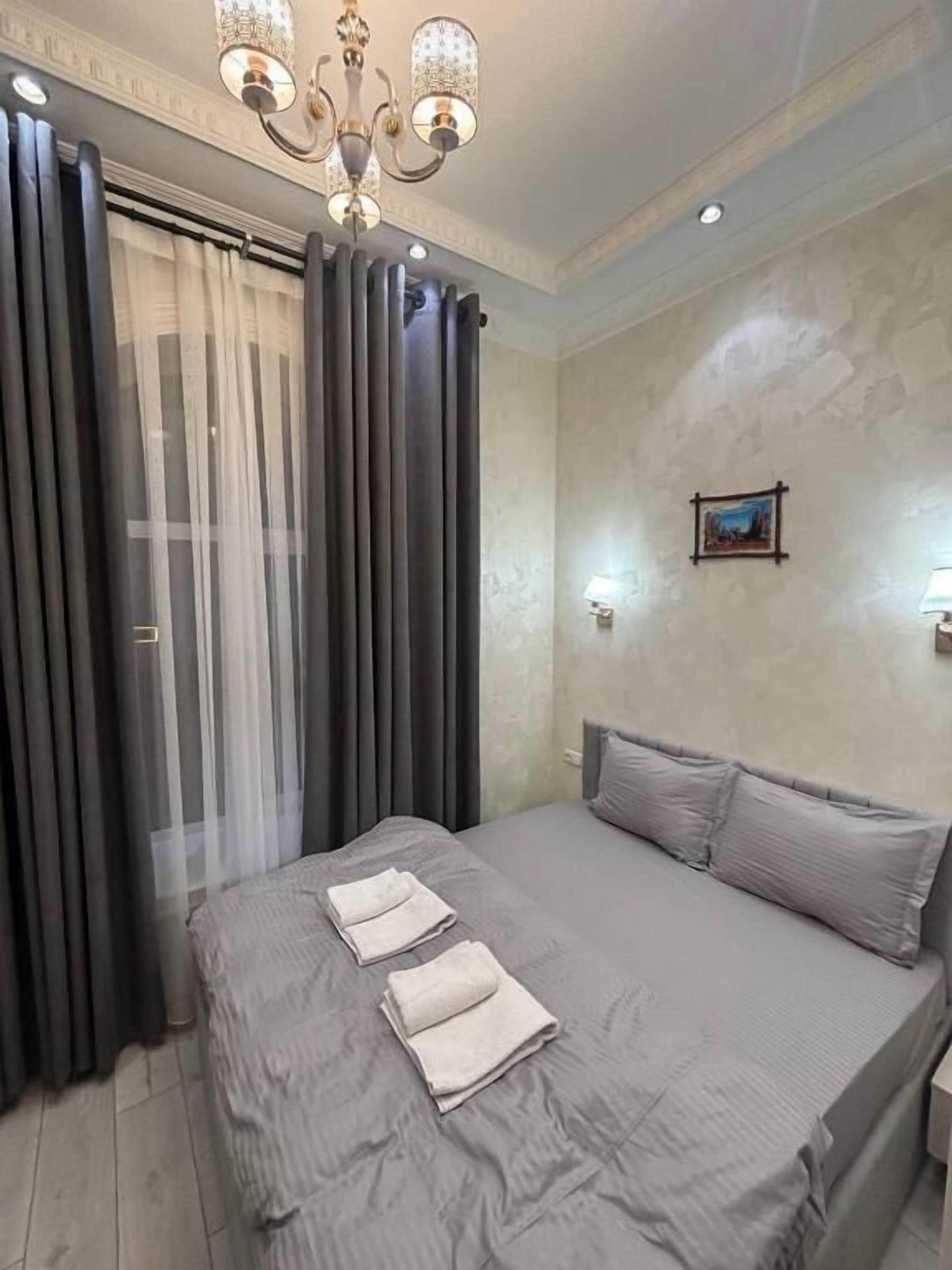 Un dormitorio con cama, cortinas, una lámpara de araña y un cuadro en la pared.