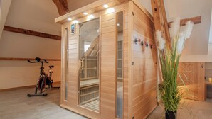 Una sauna con paredes de madera y puerta de vidrio, una bicicleta y una planta en maceta en una habitación con vigas de madera y suelo de baldosas.