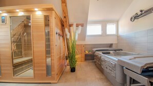 Una sauna con interior de madera, un jacuzzi de piedra y una pequeña zona de cocina con ventana.