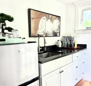 A modern kitchen with a stainless steel sink, white cabinets, a black countertop, and a framed artwork above the sink. - Phenomenal One Bedroom Cottage in Historic Old Lyme, Connecticut (Old Lyme)