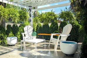 Un patio al aire libre con sillas de plástico blanco, una mesa y una maceta blanca.