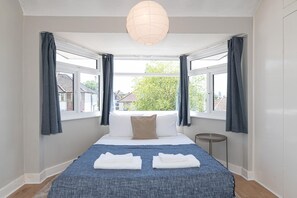 A bedroom with a bed, two windows, a bedside table, and a hanging light fixture. - Charming Home with Garden Near Wembley Stadium - Pass the Keys (London)