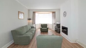 Una sala de estar con sofá, sillón, reposapiés y chimenea.