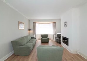 A living room with a sofa, armchair, ottoman, and a fireplace. - Charming Home with Garden Near Wembley Stadium - Pass the Keys (London)
