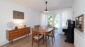 Un comedor con una mesa y sillas de madera, un armario de madera, un ventilador de techo y un piano negro.