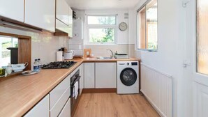 Una cocina moderna con armarios blancos, horno empotrado, lavadora y ventana que proporciona luz natural.