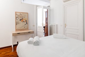 Ein Hotelzimmer mit einem Bett, einem Schreibtisch mit einem gerahmten Bild und einer Tür zu einem weiteren Raum.