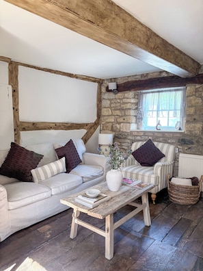 Ein gemütliches Wohnzimmer mit Sofa, Sessel und Couchtisch, Steinwand und Holzbalken.