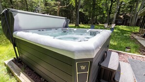 Un jacuzzi con tapa, rodeado por una terraza de madera, en una zona boscosa.