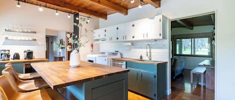 A modern kitchen with wooden cabinetry, a central island with bar stools, and a view to the dining area.