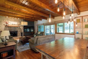 A spacious living area with a stone fireplace, wooden ceiling, and a large wooden table. - Lake & Ski House w/ Hot Tub, Firepit, and walk to the beach (Lake Harmony)