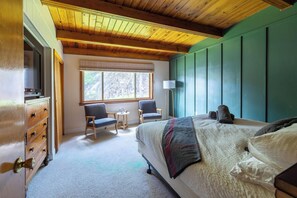 A bedroom with a wooden ceiling, a large bed, two chairs, a small table, and a window with a view of trees. - Lake & Ski House w/ Hot Tub, Firepit, and walk to the beach (Lake Harmony)