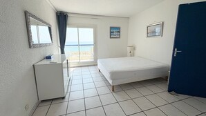 Ett sovrum med en säng, ett skrivbord, en stol, en dörr och utsikt över stranden.