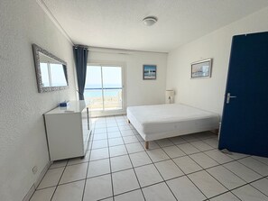Ein Schlafzimmer mit einem Bett, einem Schreibtisch, einem Stuhl, einer Tür und Blick auf den Strand.
